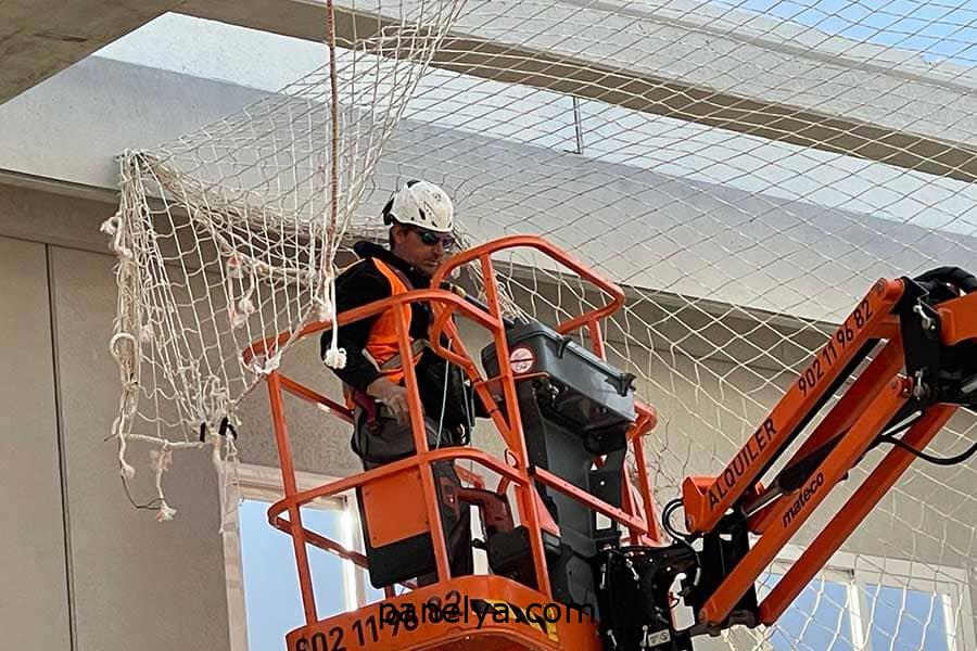 Operario colocando una red anti caídas en una obra