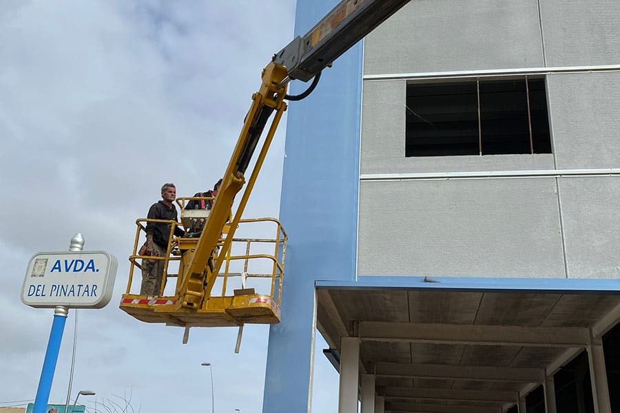 Trabajador en un elevador colocando paneles en nave industrial